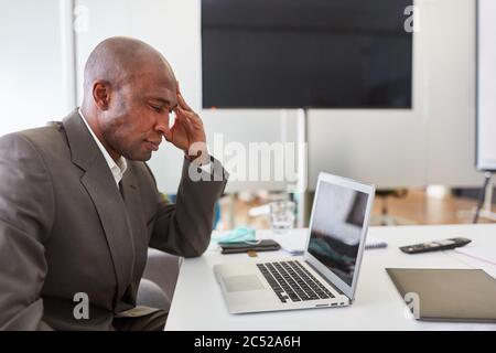 Afrikanischer Geschäftsmann als Manager denkt über ein Problem nach der Verwendung Laptop-Computer im Büro Stockfoto