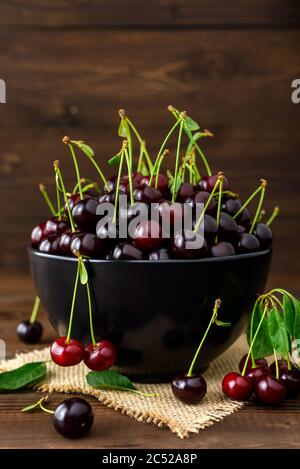 Frische Sauerkirschen in schwarzer Schale und grüne Blätter auf braunem Holztisch. Frische reife Sauerkirschen. Stockfoto