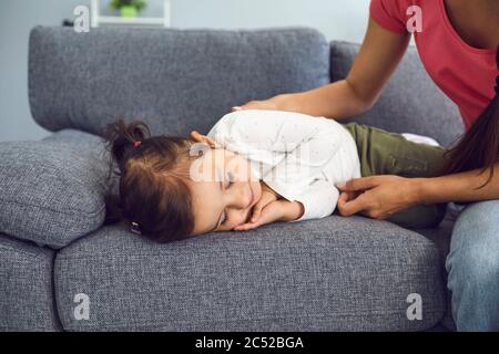 Junge Mutter in der Nähe ihrer niedlichen schlafenden Tochter auf Sofa zu Hause. Eltern beobachten liebliches Kind, das tagsüber ein Nickerchen macht Stockfoto
