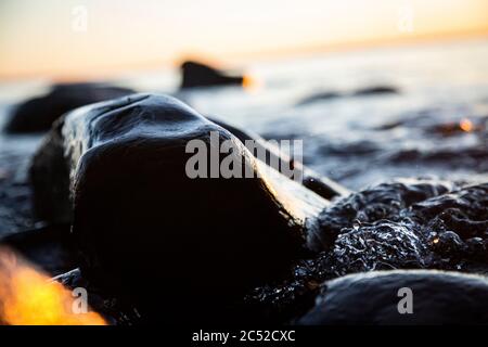 Nahaufnahme von Meereswellen, die auf einer nassen Küste brechen Steine Sommer Sonnenuntergang, Wasserspritzer, Sonnenstrahlen, Reflexionen auf Wassertropfen. Stockfoto