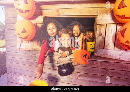 Portrait einer Gruppe von drei Kindern in Halloween Kostümen Blick aus dem Spielhaus Fenster mit Eimern für Süßigkeiten Stockfoto