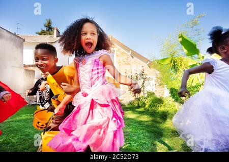 Close Portrait eines Mädchens in einer Gruppe von kleinen Kindern laufen in Halloween-Kostüm auf dem Rasen vor dem Haus Hände haltend Stockfoto