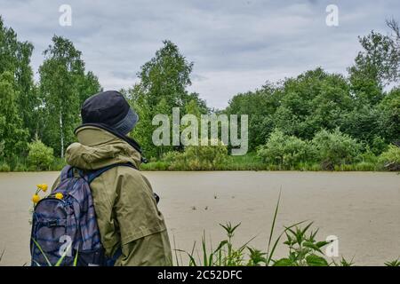 Aktiver Mann in Moskitoanzug mit Rucksack beim Wandern in der Nähe überwucherter Taiga-See in einem sibirischen Wald, Russland. Alleinreisende, Lifestyle, inländische Touris Stockfoto