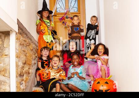Halloween Gruppe Kinder Portrait sitzen zusammen Jungen mit Mädchen auf der Treppe in der Nähe von Haus Tür in Kostümen halten Kürbis, Eimer schreien und lächeln Stockfoto
