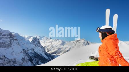 Zurück Porträt eines niedlichen Teenager-Mädchen in orange hellen Sport-Outfit mit Ski über hohe Berggipfel und blauen Himmel Stockfoto
