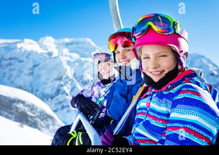 Glücklich lächelndes Mädchen sitzen auf Sessellift trägt Helm und helle Ski-Outfit mit Freunden über schönen Berggipfel Stockfoto