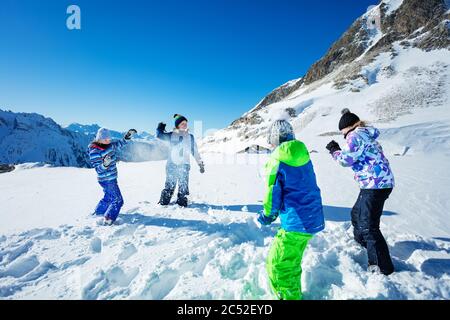 Gruppe von vier Kindern spielen Schneeballschlacht Winterspiel in den Bergen Schneewerfen und tragen Ski-Outfit Stockfoto