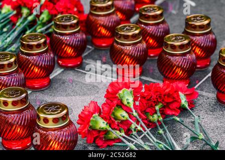 Rote Nelken auf einer Marmorplatte und Begräbnislampen. Symbol der Trauer, Blumenauflegung an der Gedenkstätte. Stockfoto