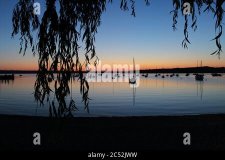 Sommeruntergang in Herrsching am Ammersee in Oberbayern, Deutschland, mit schwimmenden Booten, die von unter einer Weide gesehen werden Stockfoto