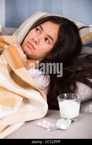 Krankes Mädchen zu Hause am Sofa in der Nähe von Pillen und Glas Milch Stockfoto