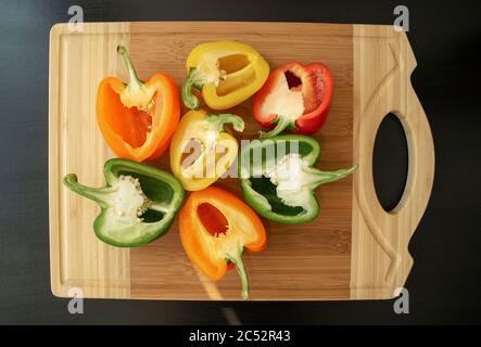 Bunte Paprika auf hellem Holzschneidebrett. Verschiedene Kapsikken auf dunklem Holztisch. Draufsicht. Paprika in Hälften geschnitten. Stockfoto