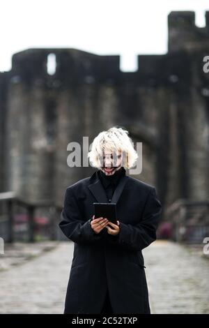 Ein edgy Millennial Mädchen in schwarz mit schwarzem Make-up steht vor dem Schloss und liest etwas auf ihrem Handy Stockfoto