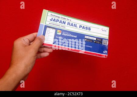 Penang, Malaysia - 25. Mai 2020 : Nahaufnahme einer Hand, die einen gebrauchten Japan Rail Pass Exchange Order auf rotem Hintergrund in Gelugor hält Stockfoto