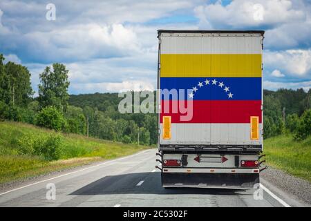 Ein LKW mit der Nationalflagge Venezuelas auf der Hintertür trägt Waren in ein anderes Land entlang der Autobahn. Konzept Export-Import,t Stockfoto