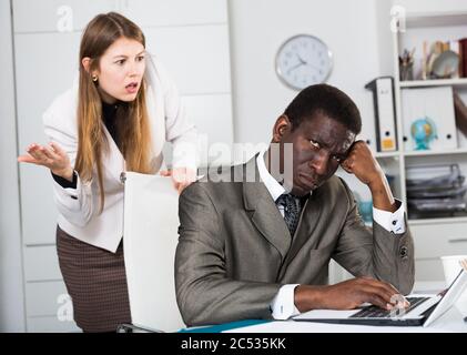 Porträt der jungen betonte Geschäftsmann im Büro mit den Unzufriedenen weiblichen Chief hinter Stockfoto