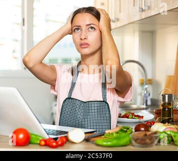Frustrierte junge Frau mit ihrem Laptop in der Küche Stockfoto