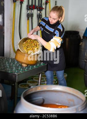 Junge workwoman füllen Gläser mit Eingelegte grüne Oliven in Verpackung Shop im Werk Stockfoto