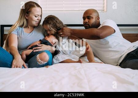 Multirassische Familie kuscheln auf dem Bett mit neugeborenem Baby Stockfoto