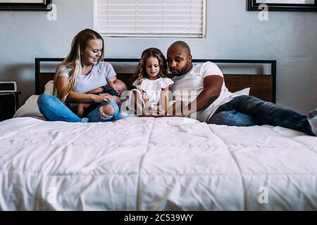Eine Familie, die sich mit einem Neugeborenen auf dem Bett kuschelt Stockfoto