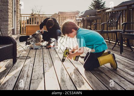 Vater und Sohn arbeiten zusammen an der Befestigung eines Decks mit Elektrowerkzeugen. Stockfoto