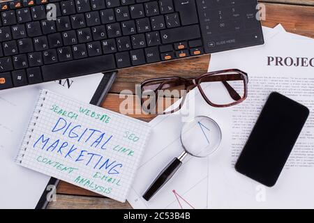 Digitales Marketing auf Notizblock und diverse Business Papers auf braunem Hintergrund. Stockfoto