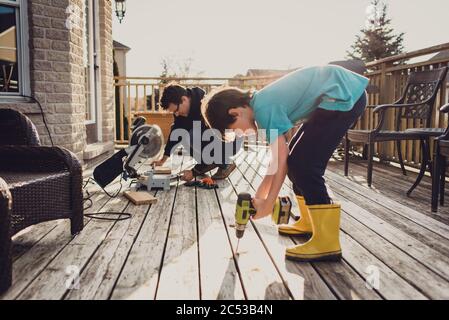 Vater und Sohn arbeiten zusammen an der Befestigung eines Decks mit Elektrowerkzeugen. Stockfoto