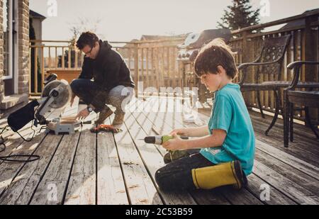 Vater und Sohn arbeiten zusammen an der Befestigung eines Decks mit Elektrowerkzeugen. Stockfoto