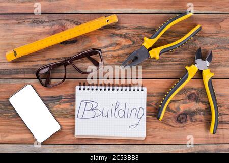 Set aus verschiedenen Bauwerkzeugen und Smartphone auf braunem Tisch. Stockfoto