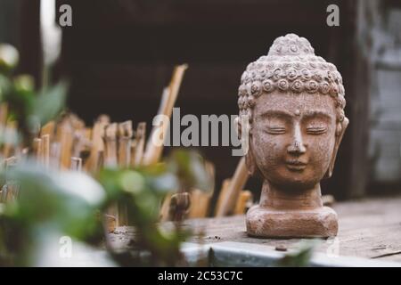 Steinbüste von Buddha auf schwarzem Holztisch mit unscharfem Hintergrund auf dem Holzboden stehend Stockfoto