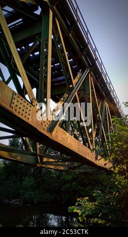 Vertikale Nahaufnahme einer verrosteten Stahleisenbahnbrücke mit Einige Bäume und Sträucher Stockfoto