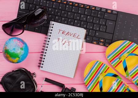 Reisetipps für Notebooks mit Accessoires für Frauen, Brille, Geldbörse und Flip-Flops auf rosa Tischplatten. Stockfoto