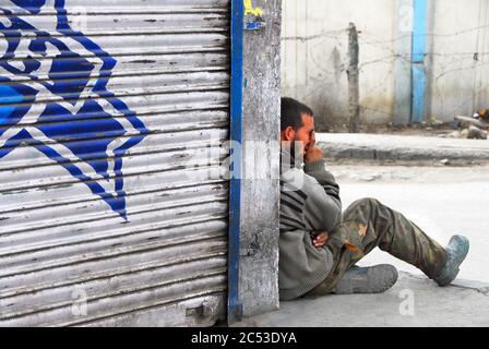 Ladakh, Indien. Ein Mann an der Seite einer Straße in einer Haltung sitzen, die an die Malerei auf den shop Shutter. Leh, Ladakh. März 17, 2014. Stockfoto