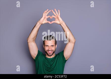 Portrait von fröhlichen Mann heben Hände zeigen Liebe Symbol Herz Form genießen 14-februar tragen grüne T-Shirt isoliert über grauen Hintergrund Stockfoto