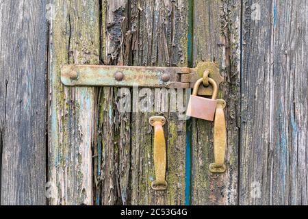 Nahaufnahme einer sehr alten verwitterten Holztür mit abblätternder Farbe mit abschließtem Vorhängeschloss und alten Griffen. Stockfoto