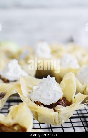 Mini-Apfelkuchen mit Phyllo-Kruste mit Schlagsahne auf einem Backgestell. Selektiver Fokus mit unscharfem Hintergrund. Stockfoto