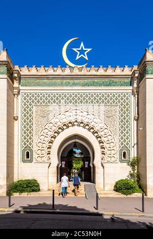 Vorderansicht der Fassade und des Tores der Großen Moschee von Paris, gekrönt von einem Stern und Halbmond, gegen blauen Himmel. Stockfoto