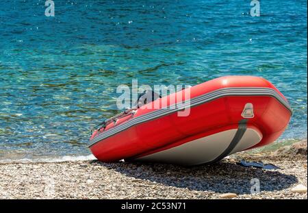 Rotes Rettungsboot, Nahaufnahme. Leeres Marine-Rettungsboot. Schlauchboot am Strand ist es rot mit einem grauen Boden und schwarzen Streifen. Stockfoto