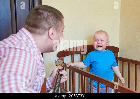 Papa spielt Gitarre, um seinen weinenden kleinen Sohn zu trösten Stockfoto