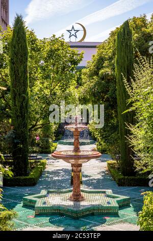 Der üppige Garten der Großen Moschee von Paris, der von Stern und Halbmond überblickt wird, ist mit Marmorbrunnen in grünen gefliesten Gassen geschmückt. Stockfoto