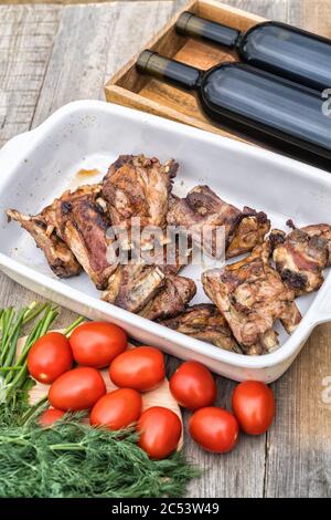 Lammrippen, auf Kohlen auf dem Grill, Wein, Tomaten und Kräutern gekocht, im Garten eines Landhauses, vertikal. Stockfoto