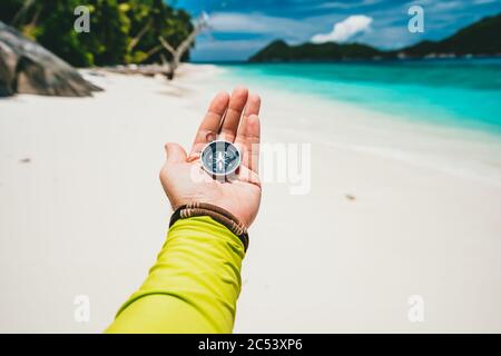 Männliche Hand hält Kompass auf tropischen Sandstrand und Meer. POV Reise Urlaub Abenteuer Konzept. Stockfoto