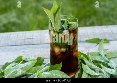 Kalter Eistee mit Minzblättern und Eis in hohem Glas auf Holztisch im Freien. Stockfoto