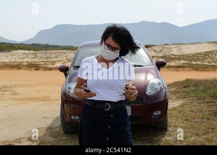 Die neue Frau mittleren Alters spricht am Strand ohne Agglomeration mit ihrem Handy und trägt eine Schutzmaske gegen Covid-19 Stockfoto