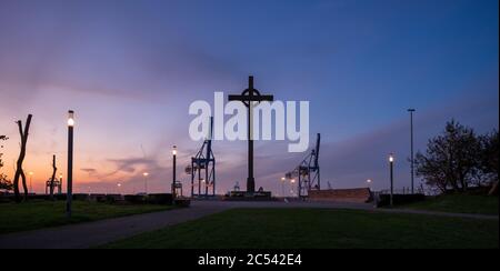 Silhouette Ansicht des Denkmals namens Visserkruis und Hafenkrane im internationalen Hafen von Zeebrugge Stockfoto