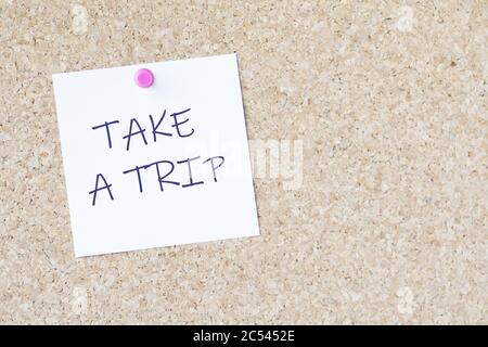 Wörter „Take a trip“ auf einem Papier, das an einem angebracht ist Platine mit einem Stift Stockfoto