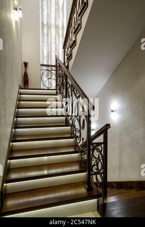 Inneneinrichtung eines Wohnhauses oder Hotels. Schöne Treppe mit LED-Leuchten. Wohndesign im modernen Stil. Moderne Holztreppe mit geschmiedetem r Stockfoto