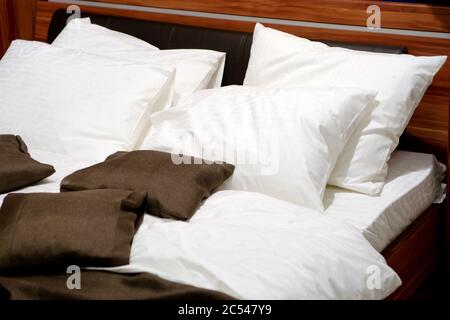 Bett mit schöner Bettwäsche. Weiße und braune Kissen und Laken. Detail der modernen Schlafzimmer-Innenausstattung. Luxuriöses, komfortables Bett im Hotel oder in der Nähe von Zuhause. Stockfoto