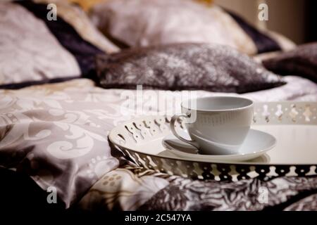 Inneneinrichtung des Hotelzimmers. Tasse Tee oder Kaffee mit einem Tablett auf einem schönen Bett. Detail eines luxuriösen gemütlichen Schlafzimmers. Wunderschöne Bettwäsche, Bettwäsche und Kissen mit verschwommenen