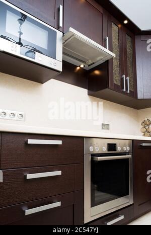 Interieur der modernen Küche. Elektrische Ausstattung der Küche. Braune Holzmöbel in der Küche. Stockfoto
