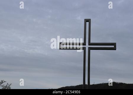 Ein katholisches Kreuz aus Metall, das auf einem Gedenkpark gebaut wurde, und ein wolkig gemachter Himmel im Hintergrund, fotografiert von unten Stockfoto